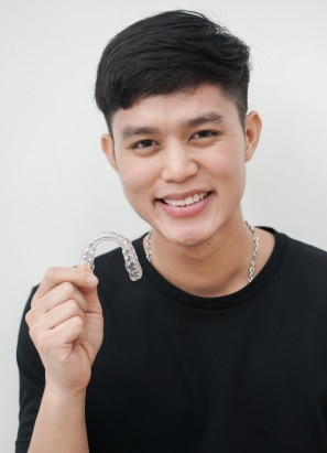 Young person with short hair and black shirt, holding up Invisalign.