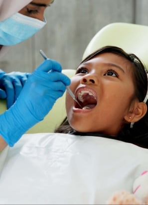 Young person lying in office chair with dentist holding dental tools before performing oral surgery.