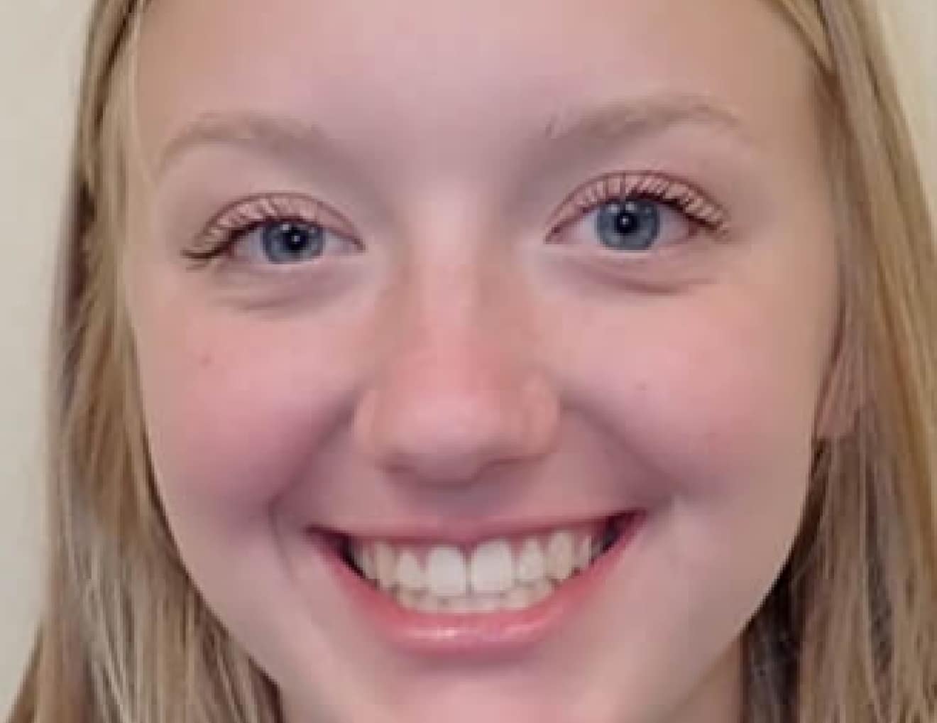 A close-up image of a smiling person with long blonde hair, blue eyes, and no visible recognizable landmarks or historical buildings in the background.