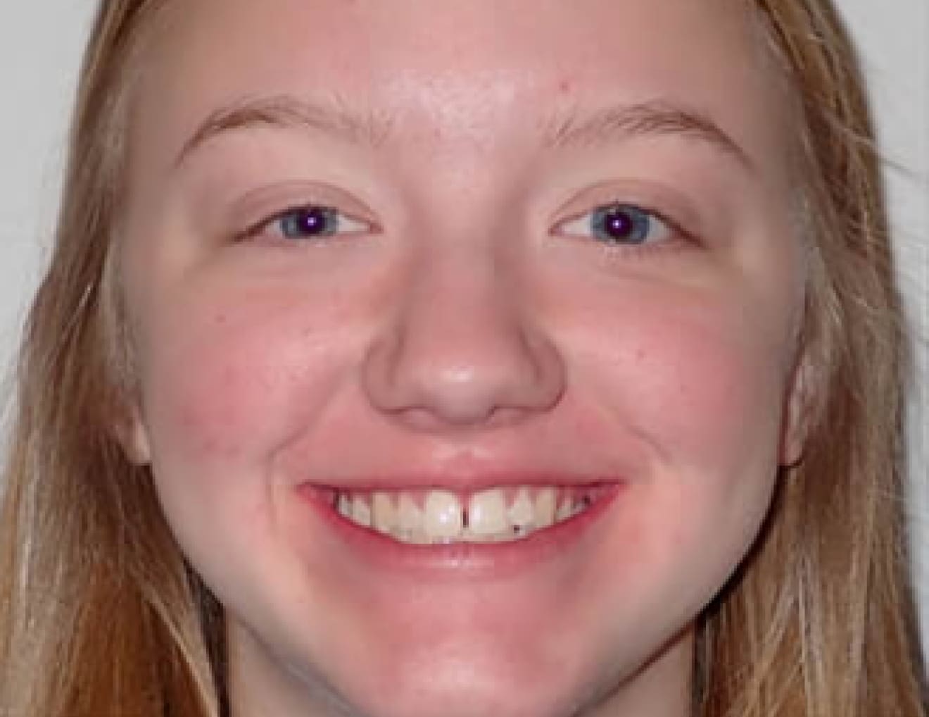 A person with long blond hair and a big smile is facing the camera against a plain background. No landmarks or historical buildings are visible.
