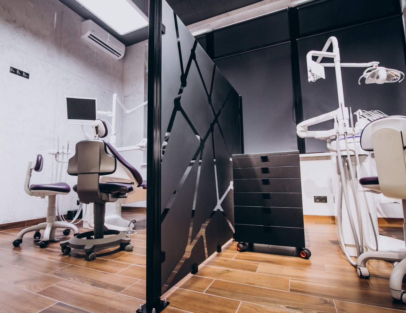 A modern dental office with purple-accented chairs, black mobile storage units, computer monitors, and dental equipment partitioned by a geometric black divider.
